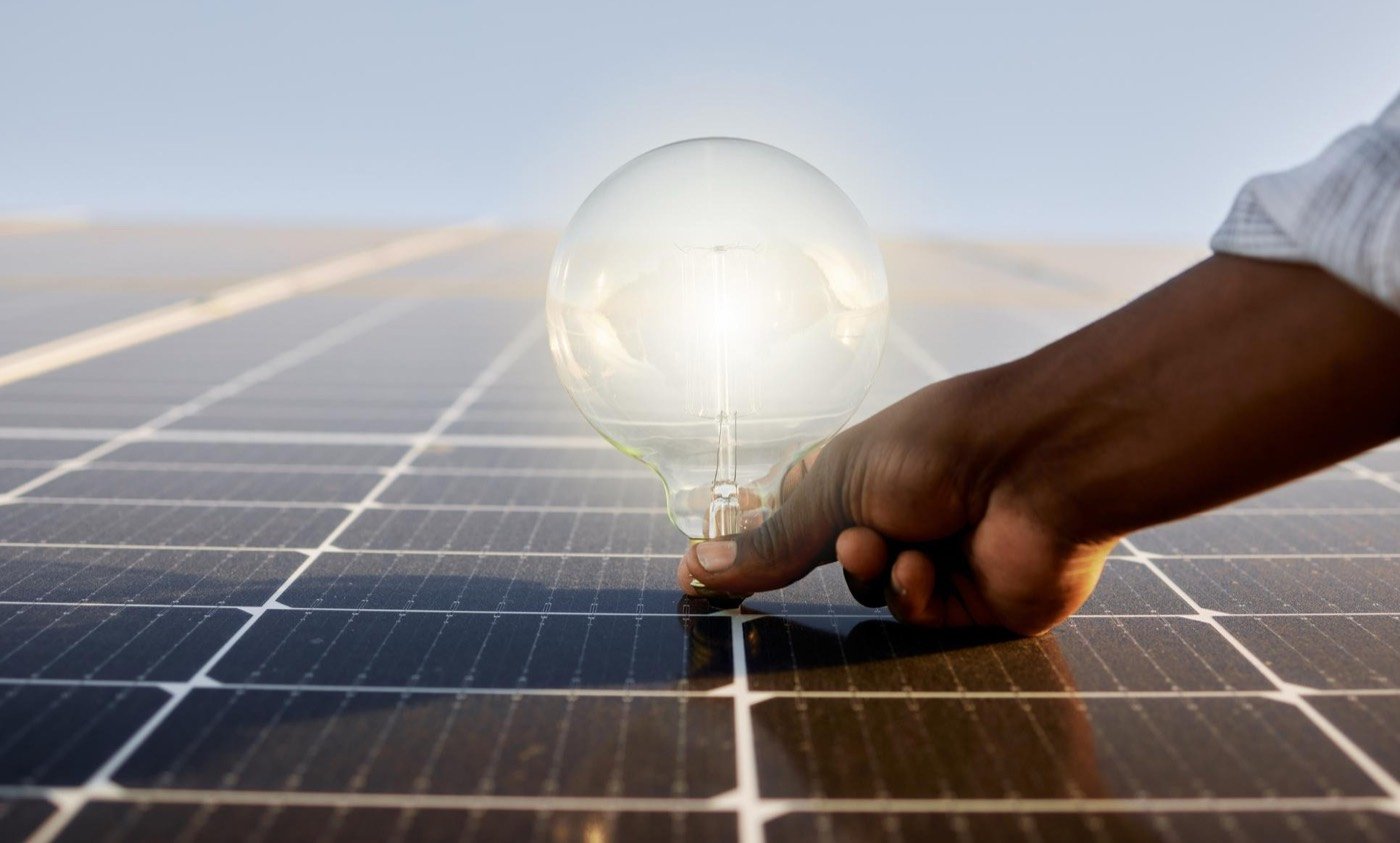 Main tenant une ampoule allumée au-dessus d'un champ de panneaux solaires