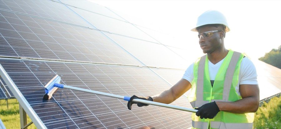Technicien nettoyant des modules photovoltaïques avec une raclette télescopique